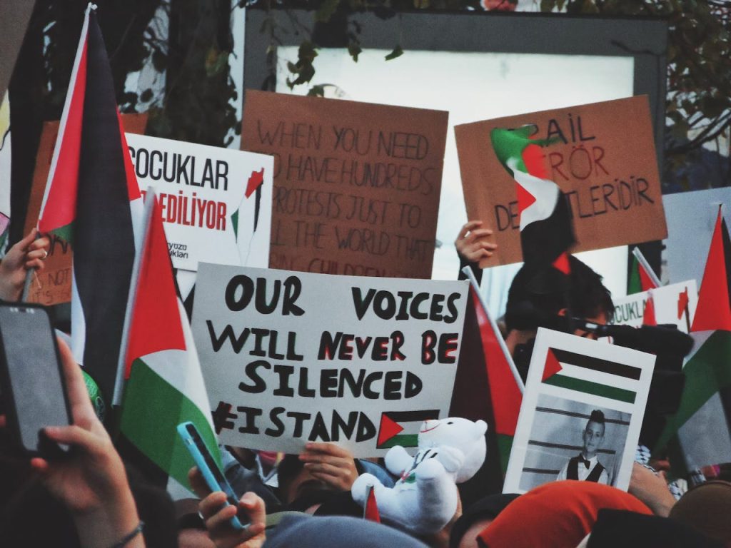 Protestors holding signs and Palestinian flags in a demonstration, advocating for their cause.